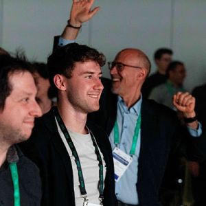 Zwei fröhliche Männer und ein jubelnder Mann im Publikum bei einem Event von Otmar Kastner